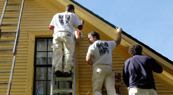A three-man paint crew topcoats a wood-sided home exterior